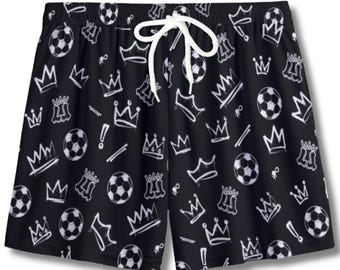 May include: Black shorts with a white drawstring and an all-over print of soccer balls, crowns, and exclamation points. The shorts have an elastic waistband and are made of a lightweight material.