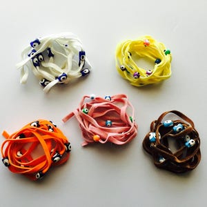 May include: Five colorful elastic cords with blue evil eye beads. The cords are white, yellow, pink, orange, and brown.
