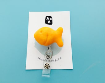 Könnte beinhalten: Ein hellgelbes, goldfischförmiges Ausweis-Jojo. Das Jojo ist an einer weißen Karte mit dem Text "A & A" und "aliandale.etsy.com" befestigt. Der Hintergrund ist hellblau.