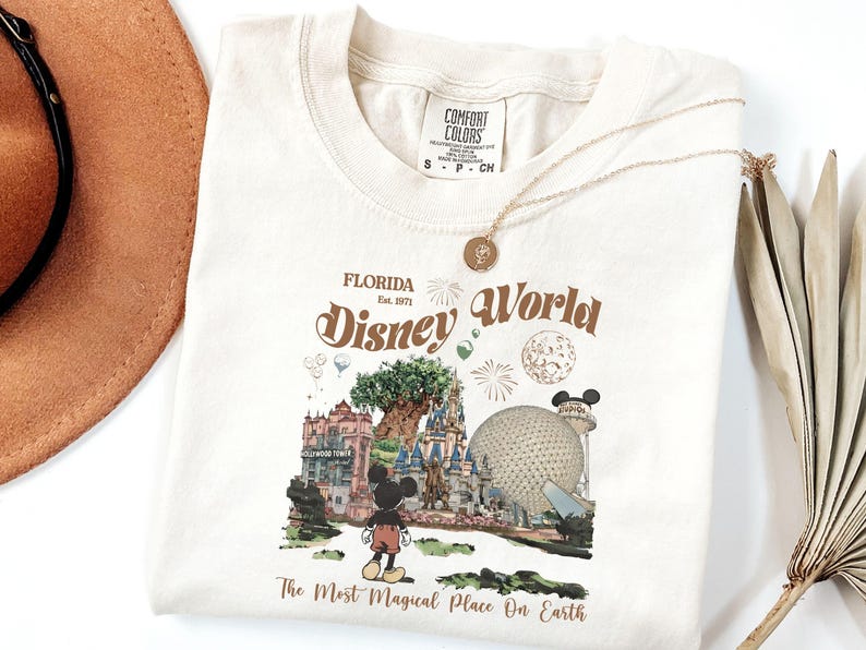 Puede incluir: Camiseta de color crema con un dise&ntilde;o gr&aacute;fico de estilo vintage de Disney World en Florida. El dise&ntilde;o incluye el texto "Florida Disney World" y "The Most Magical Place On Earth", junto con ilustraciones de lugares emblem&aacute;ticos del parque y Mickey Mouse.