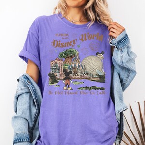 Puede incluir: Una camiseta morada con un dise&ntilde;o de Disney World en Florida. El dise&ntilde;o incluye a Mickey Mouse, Spaceship Earth y el texto "Disney World" y "The Most Magical Place On Earth".