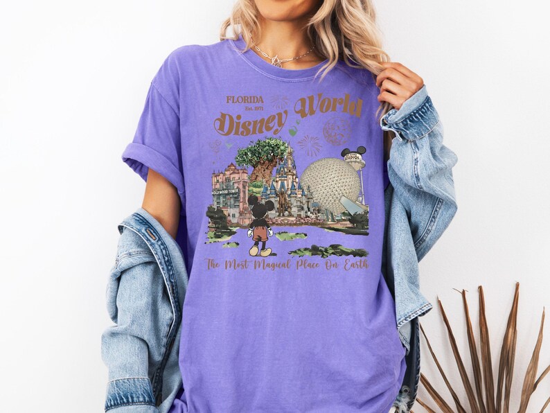 Puede incluir: Una camiseta morada con un dise&ntilde;o de Disney World en Florida. El dise&ntilde;o incluye a Mickey Mouse, Spaceship Earth y el texto "Disney World" y "The Most Magical Place On Earth".