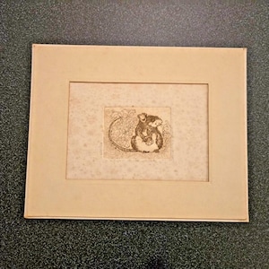 May include: A small, rectangular, cream-colored paper mat frame containing a centered, detailed black ink etching of a small rodent-like creature with a long, curved tail, positioned amidst stylized floral or leafy patterns on a textured background.