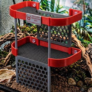 May include: A two-tier red and gray plastic observation deck for terrariums featuring a hexagonal grid pattern on the base and back panels. A silver rectangular sign on the top tier reads HIGH CLOUD OBSERVATION DECK HEX-UP CLIMBER ACCESS.