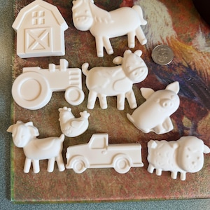 May include: A collection of nine white ceramic or plaster figurines featuring farm-themed shapes including a barn, a horse, a tractor, a cow, a pig, a goat, a chicken, a pickup truck, and a sheep, displayed next to a silver US quarter coin.