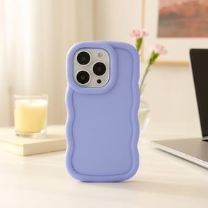 Puede incluir: Una funda de teléfono lila con un diseño de borde ondulado. La funda tiene un acabado liso y mate y un recorte para la cámara. La funda del teléfono está sobre una superficie blanca con una vela y flores en el fondo.