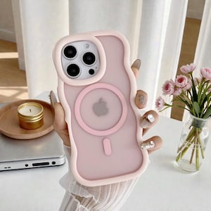 May include: A pale pink iPhone case with a wavy edge. It features a circular MagSafe charger and a small, vertical charging indicator. The case is designed for a phone with multiple camera lenses.