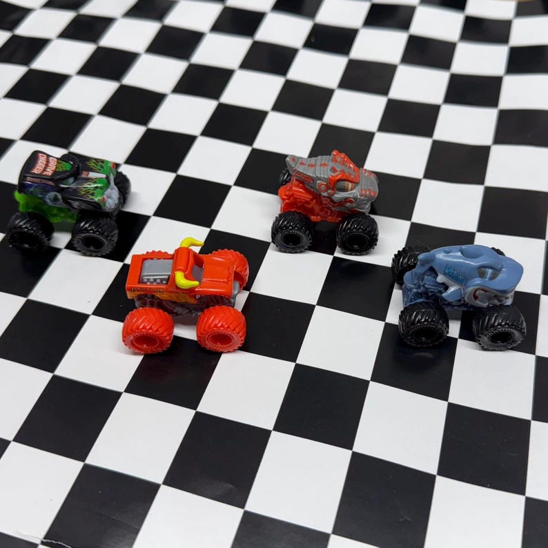 May include: Four miniature monster truck toys in various colors, including green, red, and blue, with black wheels. The trucks are arranged on a black and white checkered surface. The trucks have different designs.