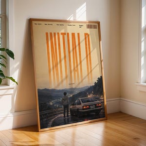 May include: A framed vertical poster featuring the text INITIAL D in large orange letters at the top. Below, a person stands on a winding mountain road at night next to a white hatchback car, with a landscape of dark hills and distant city lights.