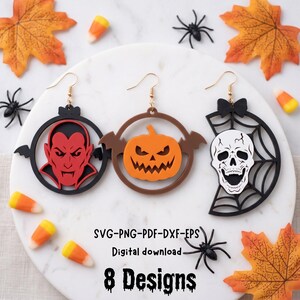 May include: Three dangling earrings featuring Halloween motifs: a red vampire in a black circle, an orange pumpkin in a brown circle, and a white skull in a black spiderweb. The text reads: SVG-PNG-PDF-DXF-EPS Digital download 8 Designs.