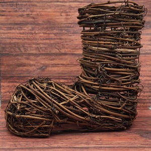 May include: A decorative boot-shaped object crafted from interwoven brown twigs and vines. The boot features a tall, cylindrical shaft and a rounded foot, all constructed with natural materials. The rustic design is set against a wooden background.