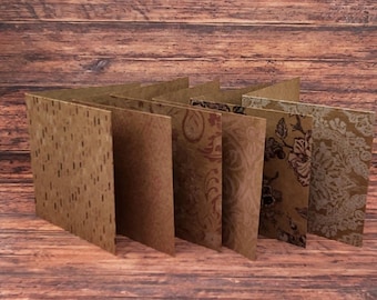 May include: A handmade, multi-panel card with various patterned paper pages. The pages display a range of designs, including a speckled pattern, swirling motifs, and floral prints in shades of brown and beige. The card is displayed on a wooden surface.