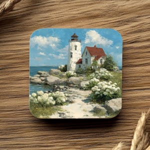 May include: Square coaster with a coastal landscape painting. The artwork shows a white lighthouse with a red roof, set against a blue sky with fluffy clouds. White flowers and rocky terrain surround the lighthouse, with the sea in the background.