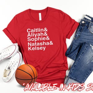 May include: A red t-shirt with the names Caitlin, Aliyah, Sophie, Natasha, and Kelsey in white text. The shirt is paired with blue jeans, white sneakers, and a basketball. Available in kids sizes.