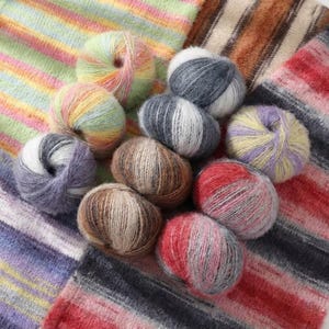 以下が含まれることがあります： 緑、黄色、ピンク、紫、グレー、茶色など、さまざまな色合いのカラフルな毛糸玉のコレクション。 毛糸はストライプの生地の背景に配置されており、編み物や編み物プロジェクトに最適です。