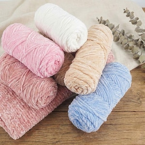 May include: A collection of soft, colorful yarn skeins in various shades. The assortment includes pink, white, beige, and blue yarn. The yarn has a velvety texture, suggesting it is made from a plush material, perfect for knitting or crocheting projects.