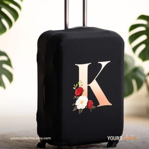 May include: Black suitcase cover with a large, gradient-coloured letter "K" and a floral arrangement of red and white flowers. The cover is designed to fit a standard suitcase and has a sleek, modern look.