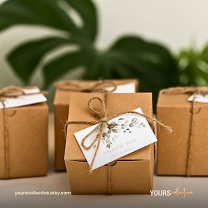 May include: Several small, brown cardboard gift boxes tied with twine. Each box has a white tag with the words "THANK YOU" and a floral design. The boxes are arranged in a group, suggesting a wedding or party favor.