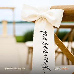 Op de afbeelding: Een crèmekleurig lint met het woord "reserved" in zwart schrift is vastgebonden aan een houten stoel. Het lint is geknoopt tot een grote strik. De achtergrond is wazig en toont een omgeving aan het water, wat duidt op een bruiloft of een speciale gebeurtenis.