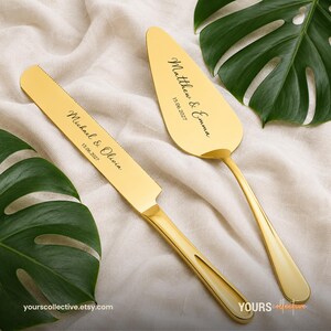 Puede incluir: Un juego de cuchillo y pala para pastel en tono dorado con acabado pulido. El cuchillo está grabado con el texto Michael & Olivia 15.06.2027, y la pala está grabada con el texto Matthew & Emma 15.06.2027 en una fuente de estilo cursiva.