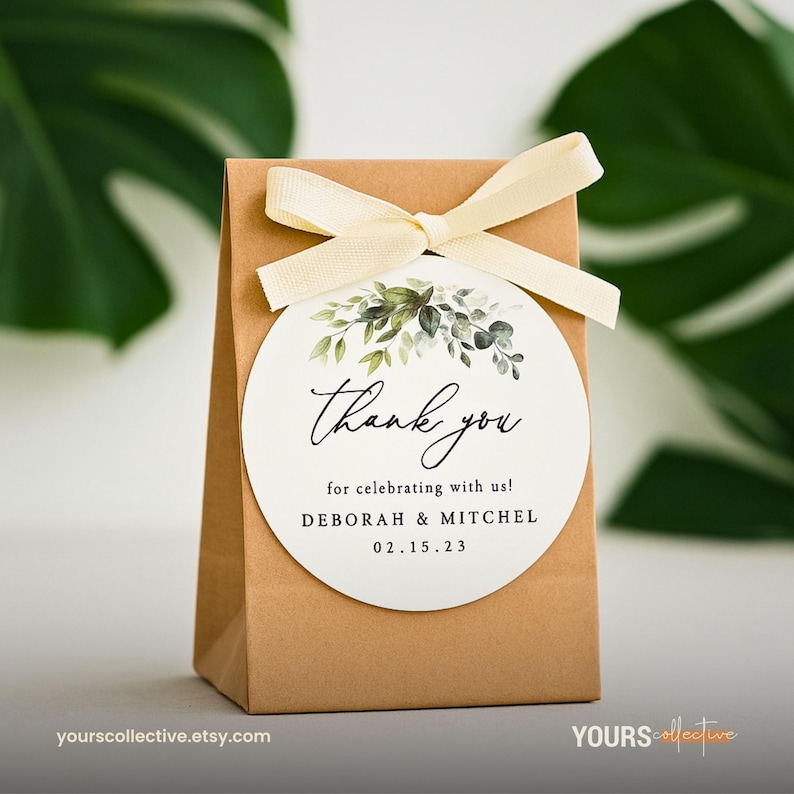 May include: A small brown paper gift bag tied with a cream-colored ribbon. A white circular tag is attached, featuring the words "Thank you" in elegant script, with botanical illustrations and the names Deborah & Mitchel, and the date 02.15.23.