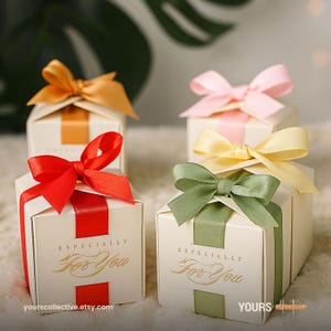 Könnte beinhalten: Elfenbeinfarbene Geschenkboxen mit farbigen Satinbändern und Schleifen in Rot, Rosa, Gelb, Grün und Orange. Jede Box trägt den goldenen Schriftzug "Especially For You". Die Boxen sind auf einer weichen, strukturierten Oberfläche angeordnet.