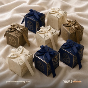 May include: A collection of seven square gift boxes in navy blue, cream, and metallic gold, each featuring a decorative floral pattern and a matching satin ribbon tied in a bow on top. The boxes are arranged in a cluster, displaying various colour combinations.