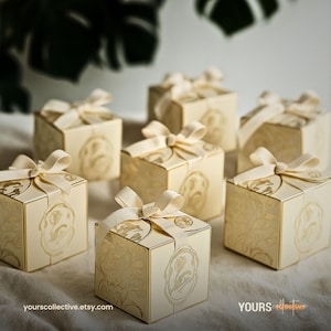 Puede incluir: Varias cajas de regalo color crema con diseños florales y de pájaros atadas con cintas color marfil. Las cajas están dispuestas sobre una superficie neutra. La URL de la tienda Etsy es visible.