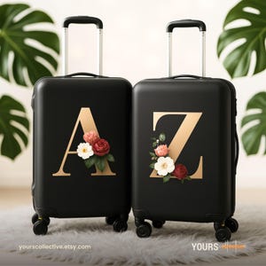 May include: Two black rolling suitcases with gold letters "A" and "Z" and floral arrangements. The suitcases have extendable handles and wheels. The Etsy shop URL is visible at the bottom.