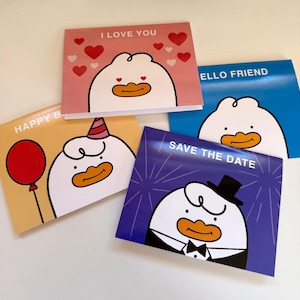 May include: A collection of greeting cards with a cartoon duck design. The cards feature phrases like "I Love You," "Hello Friend," "Happy B," and "Save the Date." Each card has a different background color, including pink, blue, yellow, and purple.