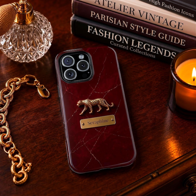 May include: A dark red, marble-patterned smartphone case featuring a gold-toned leopard figurine and a rectangular gold-toned metal plaque engraved with the name Seraphine, positioned centrally on the back of the device case.
