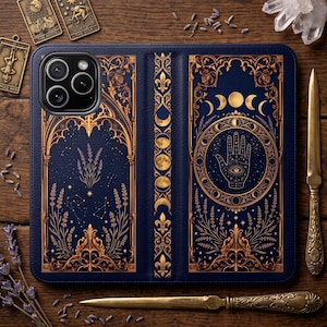 May include: A dark blue wallet-style phone case featuring intricate gold foil illustrations of a hamsa hand, lunar phases, constellations, and floral motifs. The design includes ornate gothic-style arches and decorative fleur-de-lis patterns.