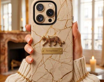 May include: A beige phone case with a gold marble pattern, featuring a three-dimensional gold leopard figure and a rectangular gold nameplate engraved with the text Seraphine. The case has a black camera lens frame and a gold chain strap.