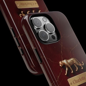 May include: A dark red marble-patterned phone case featuring a gold-toned leopard figurine and a rectangular gold nameplate engraved with the name Charlotte. The case has a black camera cutout and side buttons, with a glossy finish throughout.