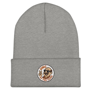 Może przedstawiać: Szara czapka beanie z wywiniętym brzegiem. Czapka posiada okrągłą naszywkę z kreskówkowym wizerunkiem mężczyzny w okularach przeciwsłonecznych i wąsach, pokazującego znak pokoju. Tekst "UNC AT THE FUNC" otacza obraz.