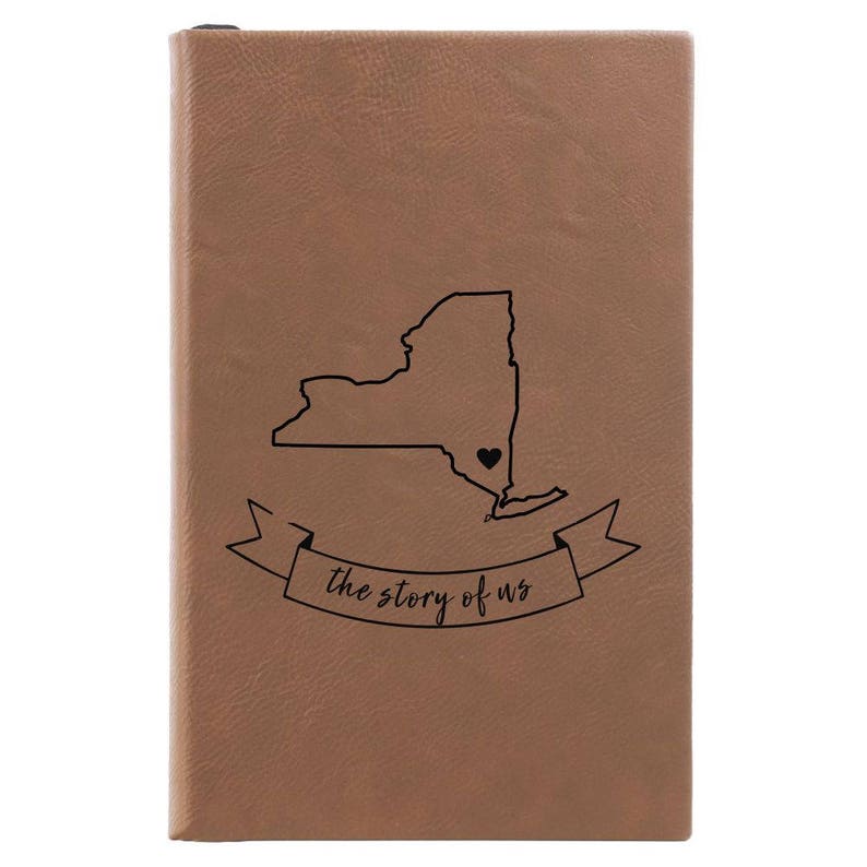 Peut inclure: Un journal en cuir marron avec un contour noir de l'&eacute;tat de New York et un petit c&oelig;ur au centre. Le journal a une banni&egrave;re qui dit "the story of us".