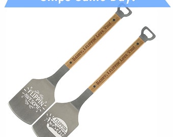 May include: Two wooden handled spatulas with metal blades. The blades are engraved with the text "Flipping Awesome" and the handles are engraved with the text "Daddy, I Flipping Love You!" Each spatula has a bottle opener on the end of the handle.