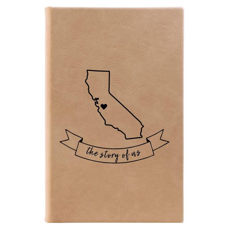 Peut inclure: Un journal en cuir beige avec un contour noir de l'&eacute;tat de Californie et un c&oelig;ur au centre. Le journal a une banni&egrave;re qui dit "the story of us".