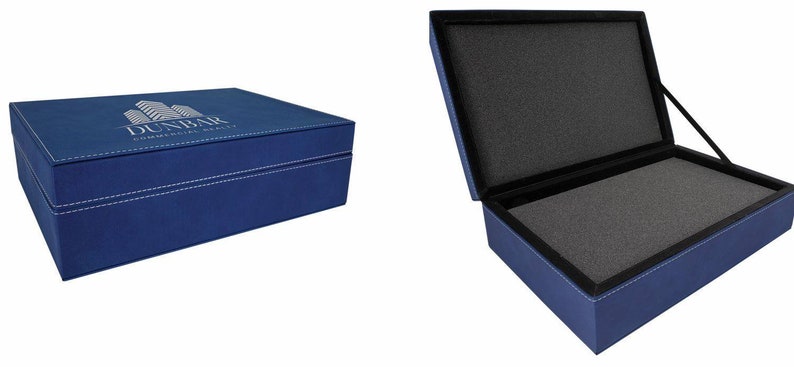 May include: A blue faux leather box with a white logo that says "Dunbar Commercial Realty" and a building graphic. The box is open to reveal a grey foam interior.