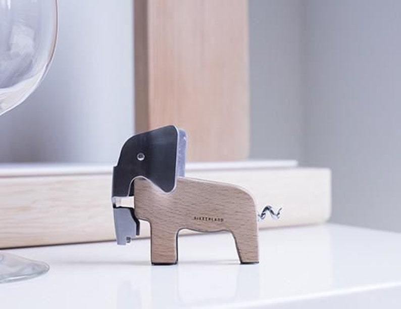 Puede incluir: Un sacacorchos de madera con forma de elefante con una cabeza de metal plateado y una cola de metal plateado. El sacacorchos est&aacute; etiquetado como "JAERTHLAND".