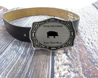 Puede incluir: Una hebilla de cinturón de plata con un diseño ornamentado. La hebilla presenta una silueta de un cerdo y el texto "YOUR TEXT HERE".