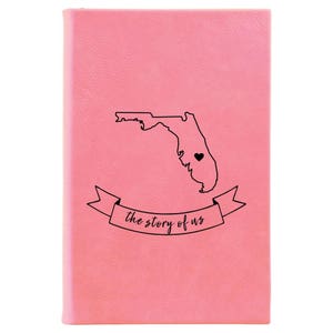 Peut inclure: Un carnet en cuir rose avec un contour de l'&eacute;tat de Floride et un c&oelig;ur au centre. Le texte "the story of us" est &eacute;crit sur une banni&egrave;re sous l'&eacute;tat.