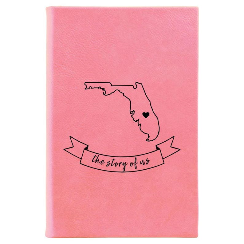 Peut inclure: Un carnet en cuir rose avec un contour de l'&eacute;tat de Floride et un c&oelig;ur au centre. Le texte "the story of us" est &eacute;crit sur une banni&egrave;re sous l'&eacute;tat.