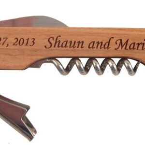 K&ouml;nnte beinhalten: Ein Flaschen&ouml;ffner mit einem Holzgriff, einem Korkenzieher und einem Flaschen&ouml;ffner. Der Griff ist mit dem Text "July 27, 2013 - Shaun and Maria" graviert.