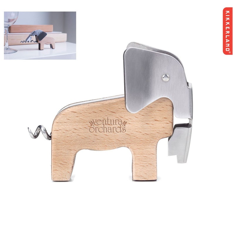 Puede incluir: Un abridor de botellas de madera con forma de elefante con una cabeza de metal plateado y una cola de sacacorchos. El abridor tiene las palabras "ventura orchards" grabadas en el lateral.