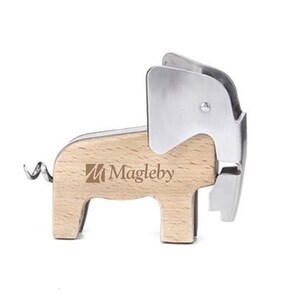 Puede incluir: Un abridor de botellas de madera con forma de elefante con un sacacorchos de metal plateado y un cortador de papel de aluminio. El abridor tiene el texto "Magleby" impreso en el lateral.