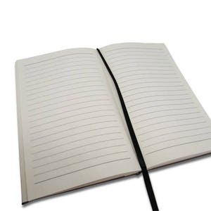 Peut inclure: Un carnet &agrave; couverture blanche ouvert avec des lignes et un ruban noir en guise de marque-page. Le carnet est pos&eacute; &agrave; plat sur une surface blanche.