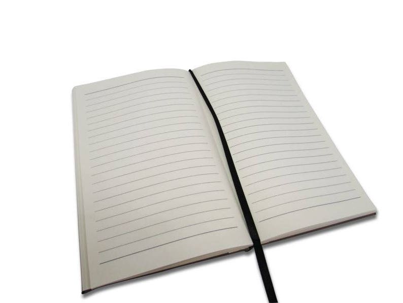 Peut inclure: Un carnet &agrave; couverture blanche ouvert avec des lignes et un ruban noir en guise de marque-page. Le carnet est pos&eacute; &agrave; plat sur une surface blanche.