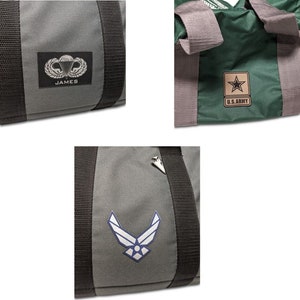 Op de afbeelding: Drie grijze reistassen met verschillende militaire emblemen. De eerste tas heeft een parachute-embleem met het woord "JAMES" eronder. De tweede tas heeft een blauw Air Force-embleem. De derde tas heeft een groen U.S. Army-embleem met een ster.