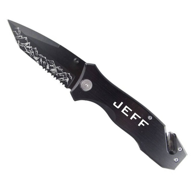 May include: Black pocket knife with a serrated blade and a safety feature. The knife has a mountain range design on the blade and the name "JEFF" engraved on the handle.